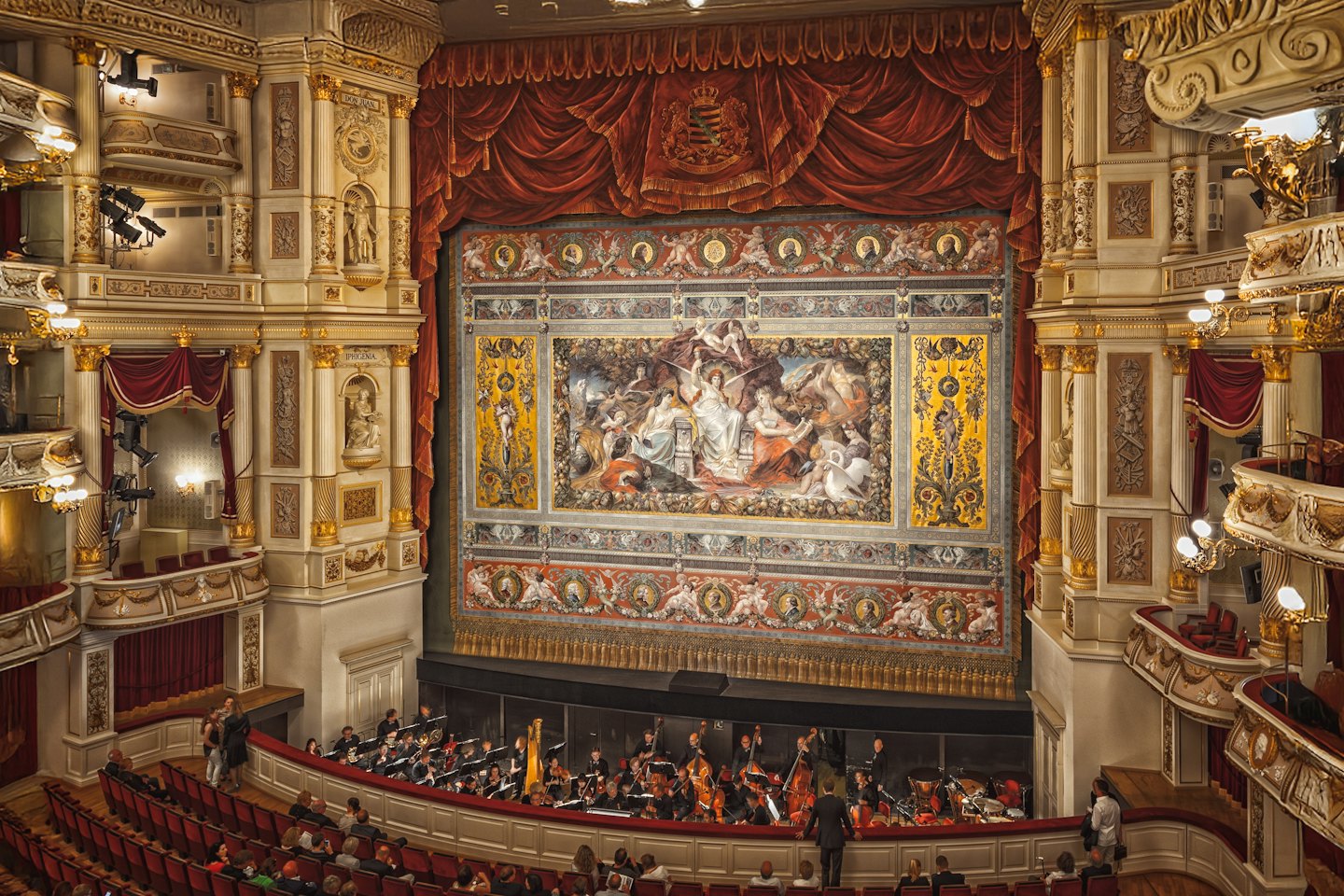 Interno del teatro dell'opera con orchestra che si esibisce sul palco.